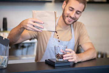Smiling man at bar pouring coffee beans