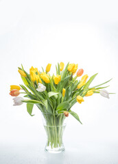 bouquet of yellow bright tulips in a glass transparent vase on a white background.
