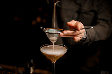 close-up view on sieve through which male bartender pours frothy espresso martini cocktail into...