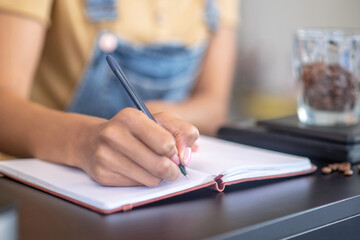 Female hand writing with pen in notebook on counter