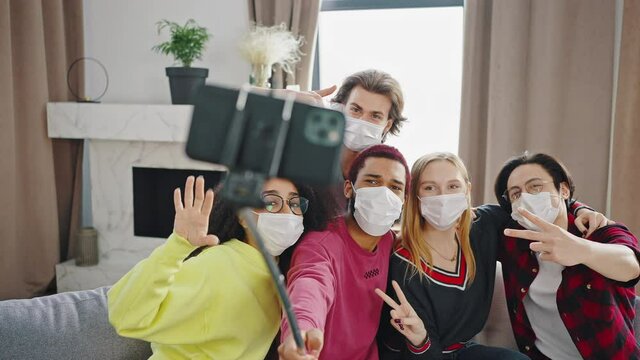 Group of mixed race friends making selfie celebrating at home with medical protection mask. Happy people indoor are having party at the coronavirus new normality time
