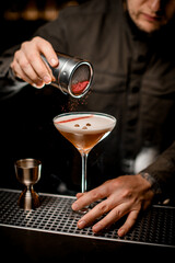 male bartender gently sprinkles colored powder on foam of espresso martini cocktail in glass