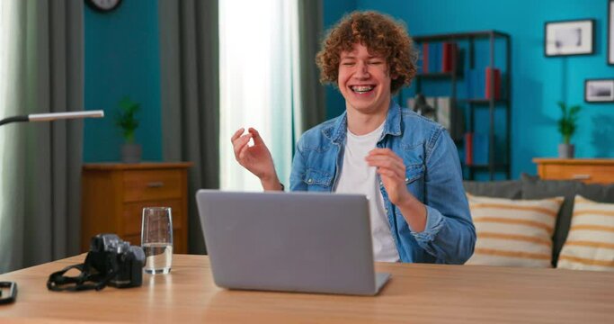 Successful teenage boy sits at table uses laptop read e-mails online home office, gets good news, positive exam results, new opportunity, feels joy triomphe, celebrates victory, happy dancing