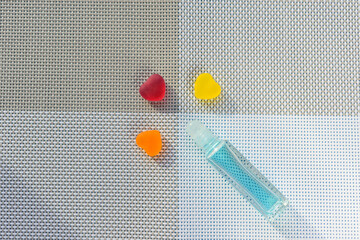 Glass bottle. Ball dispenser for perfume. Liquid color - Morning Glory. Three hearts, color - red, yellow, orange. Background is a textured four-area woven fabric.