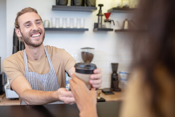 Fototapeta na wymiar Enthusiastic man giving takeaway coffee to customer
