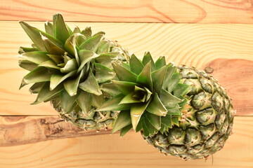 Two organic juicy pineapples on a wooden table, close-up, top view.