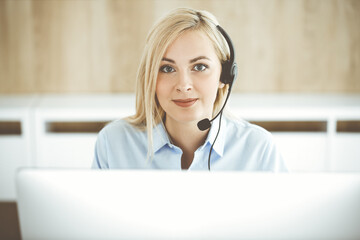Blonde business woman sitting and communicated by headset in call center office. Concept of...