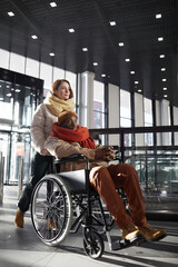Vertical full length portrait of young woman assisting African American man in wheelchair at subway station