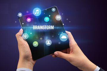 Businessman holding a foldable smartphone with BRAINSTORM inscription, social media concept