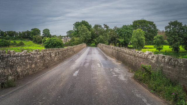 Road leading over old, 12th century stone Bective Bridge over Boyne River with stone wall on sides, Count Meath, Ireland
