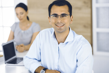 Fototapeta premium Businessman and business woman discussing questions while using a computer in modern office. Portrait of male entrepreneur at meeting. Group of diverse people