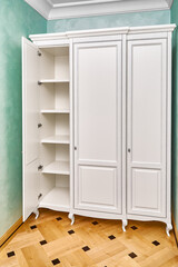 Three-section white wardrobe in classic style with inner shelves in a modern hallway with green walls and elegant wooden block parquet floor
