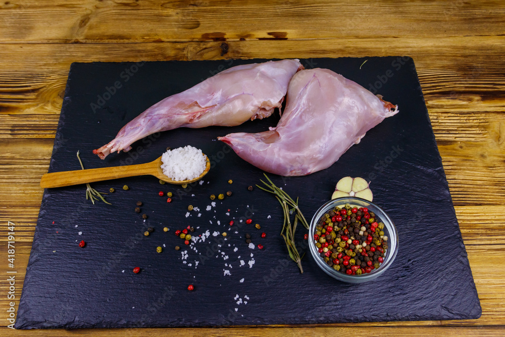 Wall mural Raw rabbit legs with spices on a black slate cutting board on wooden table