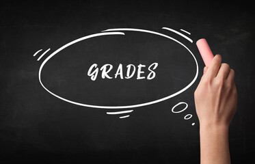 Hand drawing GRADES inscription with white chalk on blackboard, education concept