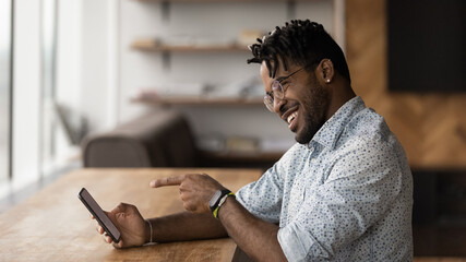 Close up smiling African American man holding phone, chatting online, making video call to friend or girlfriend, enjoying leisure time with mobile device, excited young male reading good news