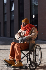 Obraz premium Vertical full length portrait of African American man using wheelchair in urban city lit by sunlight, copy space
