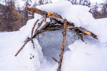 Hut made with a snowy and branches in the winter forest. Outdoor activity with children in winter concept