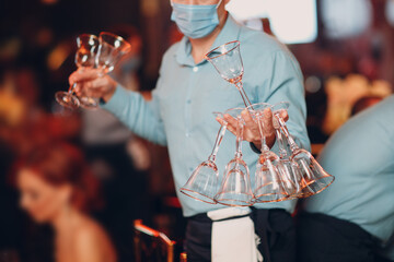 the waiter in the restaurant serves the tables and holds many transparent glasses in his hand catering concept