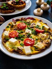 Delicious breakfast - scrambled eggs with onion, feta cheese, cherry tomatoes, champignons and chives on wooden table
