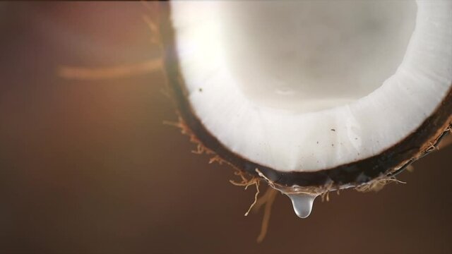Coconut milk, dripping coconut water, drops of coco nuts oil over brown background. Tropical Coco nut closeup. Healthy Food, skin care concept. Vegan food. 4K UHD video, slow motion