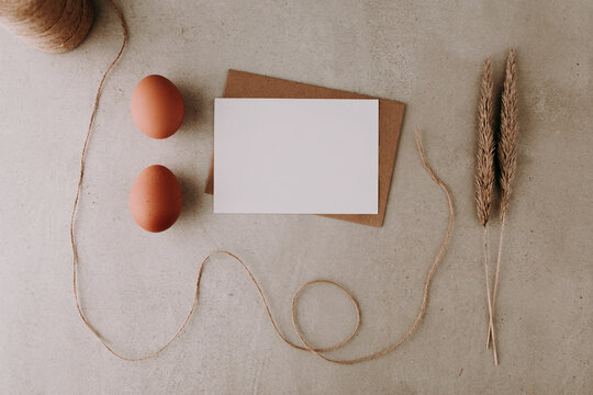 Blank white paper with two eggs, dried grass and string on grey stone background. Easter greeting card or menu list concept. Flat lay, top view.