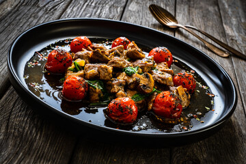 Roast veal meat with roasted tomatoes and spinach on wooden background
