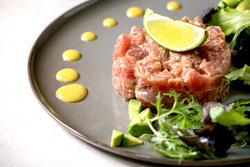 Tuna tartare with green salad, lime, avocado and mustard sauce serving on ceramic plate over white texture background. Fine dining, restaurant appetizer
