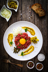 Beef tartare steak with onion, capers and pickled cucumbers on wooden table
