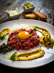 Beef tartare steak with onion, capers and pickled cucumbers on wooden table
