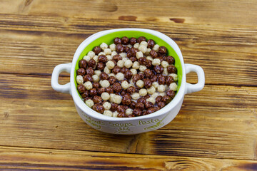 Cereal chocolate balls with milk in a bowl on wooden table