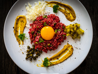 Beef tartare steak with onion, capers and pickled cucumbers on wooden table

