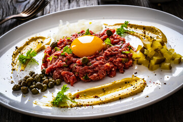 Beef tartare steak with onion, capers and pickled cucumbers on wooden table
