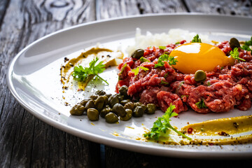 Beef tartare steak with onion, capers and pickled cucumbers on wooden table
