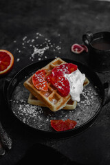 Belgian waffles with a bloody orange on a dark plate. Dark photo