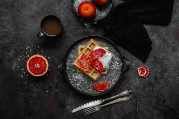 Belgian waffles with a bloody orange on a dark plate. Dark photo