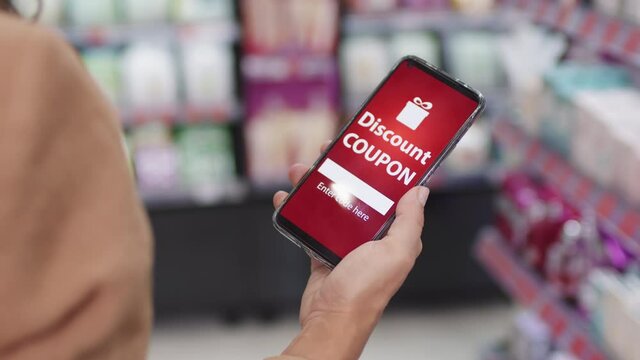 Slow-motion closeup of unrecognizable woman holding smartphone with online discount coupon standing in cosmetics store