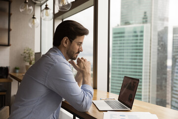 Close up thoughtful businessman wearing glasses looking at laptop screen, accountant working with...