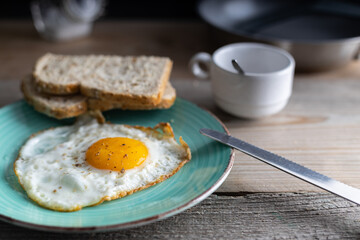 Breakfast fried sunny side up egg with whole grain bread. Fried organic egg sunny side up seasoned with salt and pepper on a plate with whole grain bread on the side. Top view.