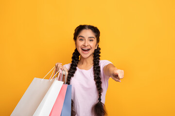 Overjoyed indian woman holding shopping bags pointing at you