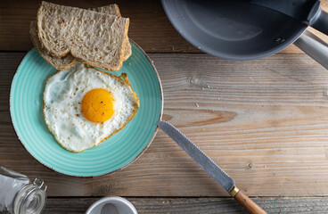 Breakfast fried sunny side up egg with whole grain bread. Fried organic egg sunny side up seasoned with salt and pepper on a plate with whole grain bread on the side. Top view.