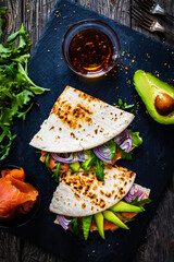 Italian piada wraps - piada stuffed with smoked salmon, avocado, arugula and onion on black stone plate 