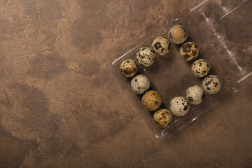 Many quail eggs in plastic packaging on brown background. Copy space.