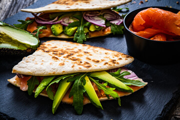 Italian piada wraps - piada stuffed with smoked salmon, avocado, arugula and onion on black stone plate 