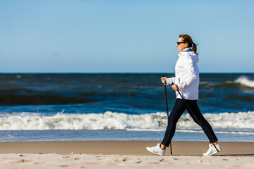 Nordic walking - middle-aged woman training on beach
