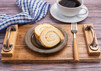 Top view of roll cake on a plate on a wooden tray with a cloth and a white coffee cup placed on a wooden table. Space for text. Concept of relaxation