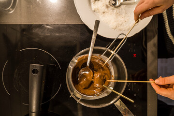 Hands over an electric induction stovetop dip chocolate balls into melted chocolate sauce before dipping into coconut flakes.