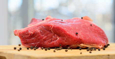 A piece of fresh beef lies on the cutting board. Sprinkled with pepper. Concept - cooking.