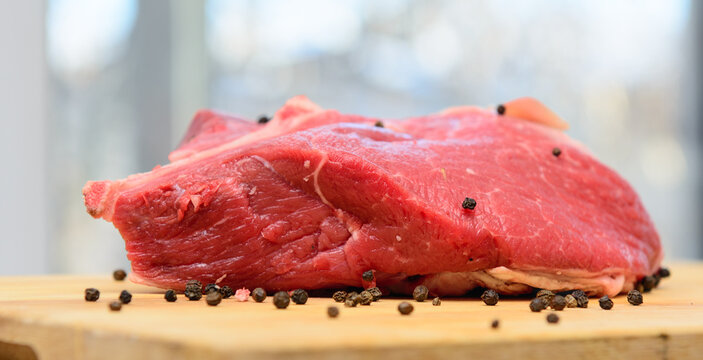 A piece of fresh beef lies on the cutting board. Sprinkled with pepper. Concept - cooking.
