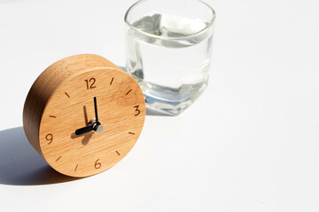 Wooden clock with glass of water on white background.