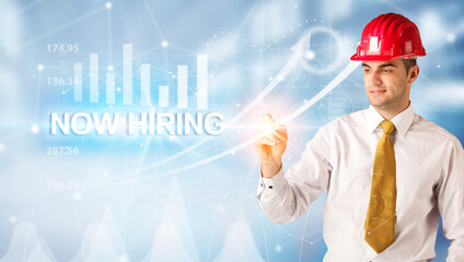 Young businessman with helmet drawing NOW HIRING inscription, modern business technology concept